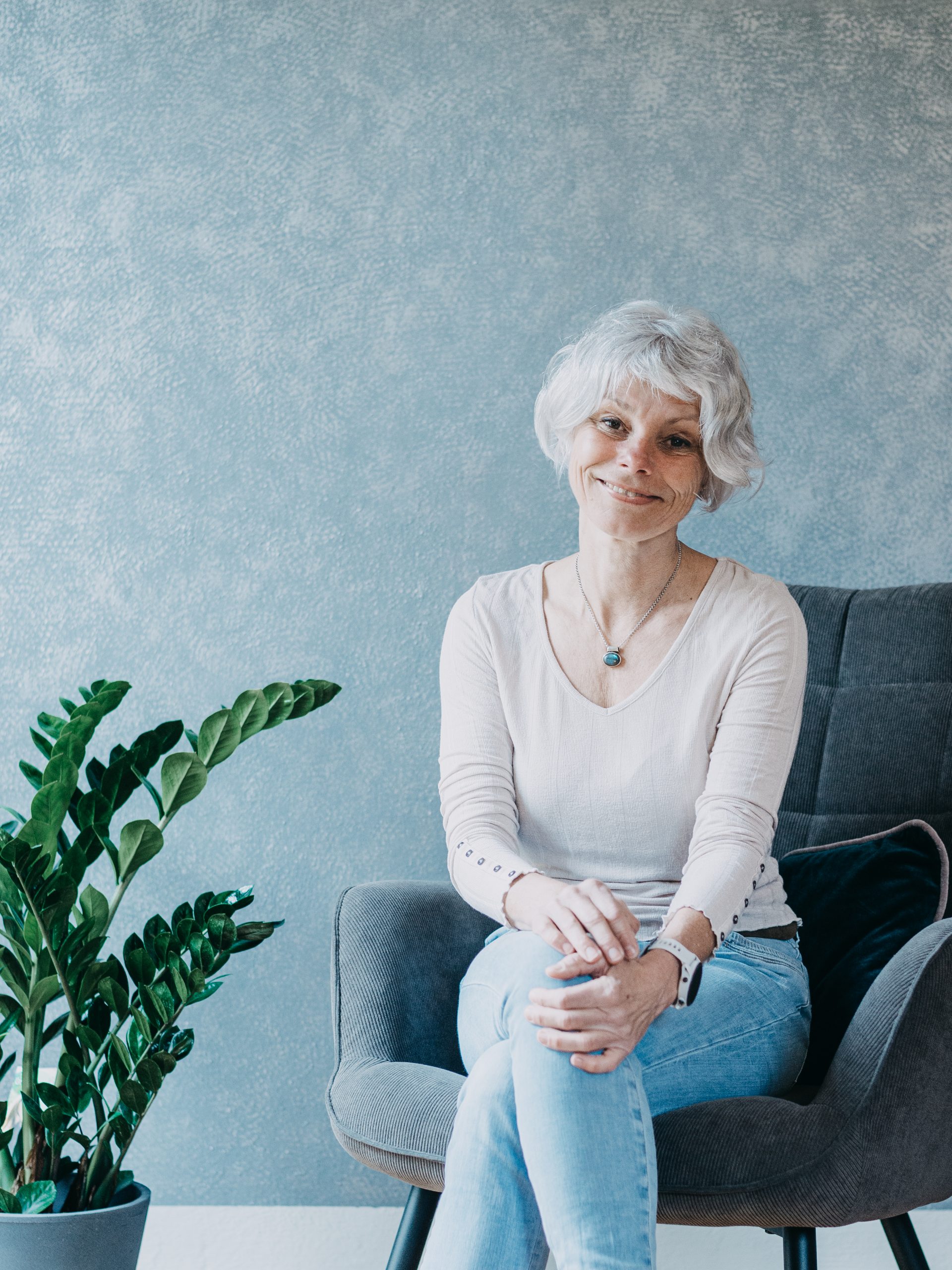 Portrait von Annemarie. Sitzend, vor einer blauen Wand.